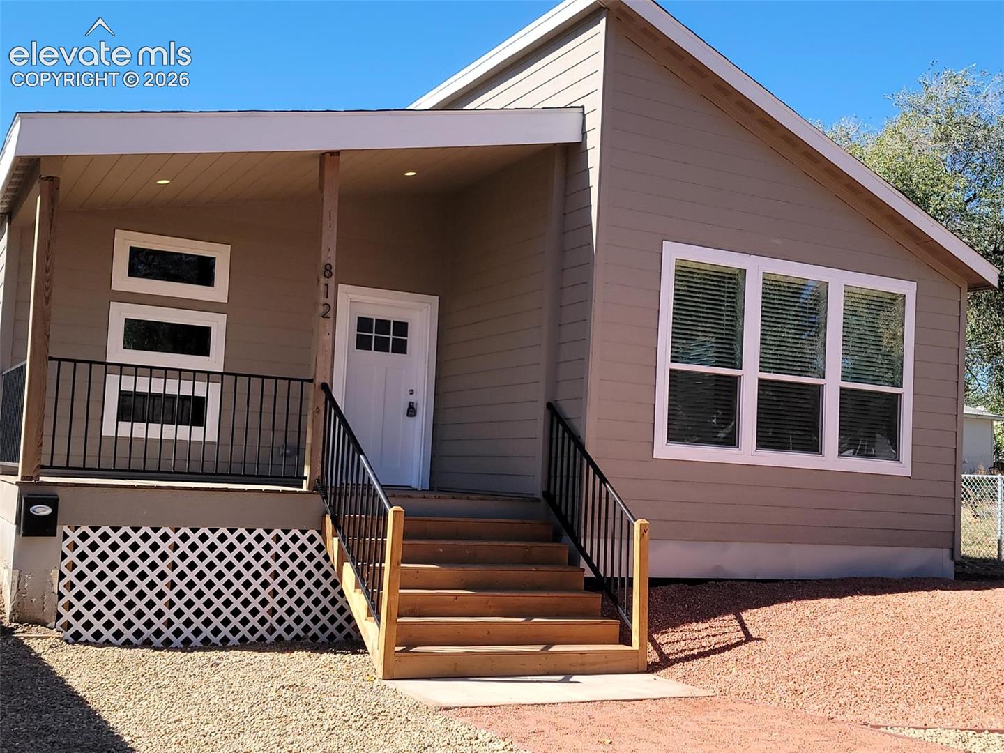 Exterior facade featuring horizontal siding, a covered front porch with recessed lighting, timber support posts, a metal railing, and a multi-pane front door