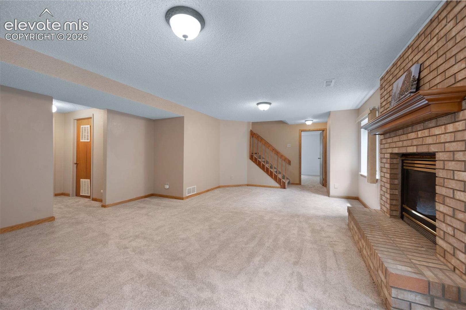 Unfurnished living room with stairway, a brick fireplace, light carpet, a textured ceiling, and baseboards