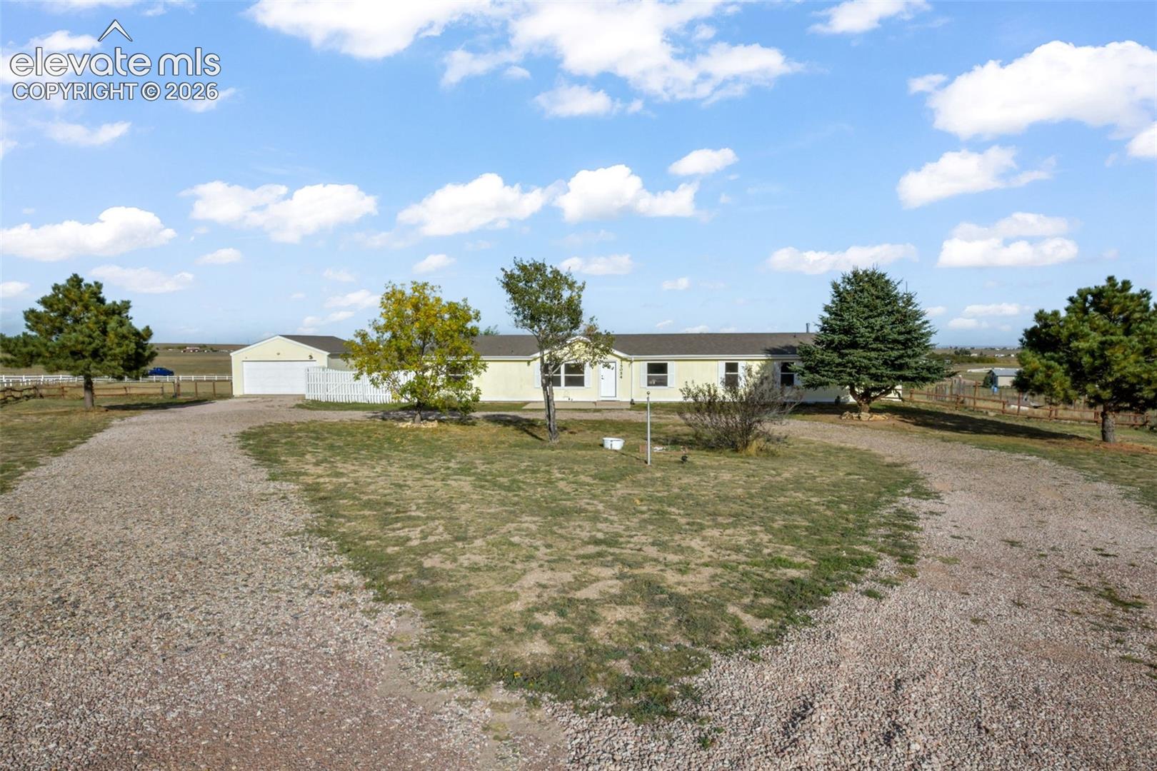 Ranch-style residence featuring a gravel driveway, detached garage with white overhead door, and a white picket fence