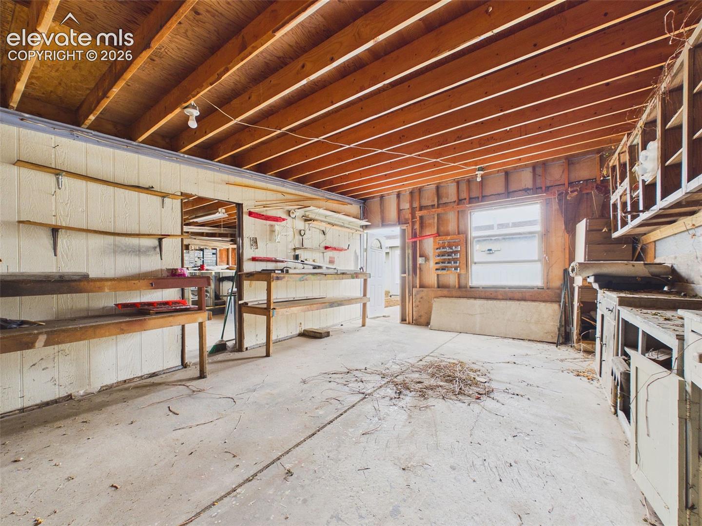 Generously sized workshop featuring exposed wood framing, concrete flooring, built-in workbenches, shelving, and natural light. Ideal for woodworking, hobbies, and projects.