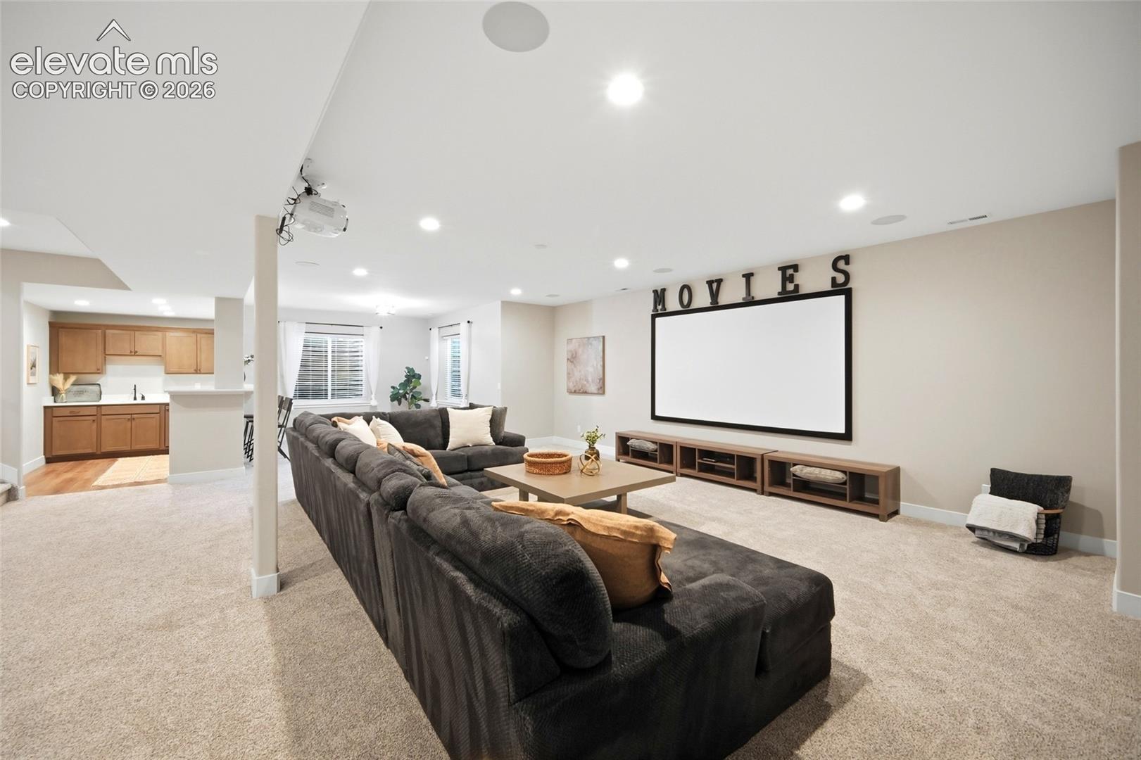 Open-concept space featuring recessed ceiling lighting, built-in projector and wall-mounted screen, integrated ceiling speakers, and a wet bar with wooden cabinetry