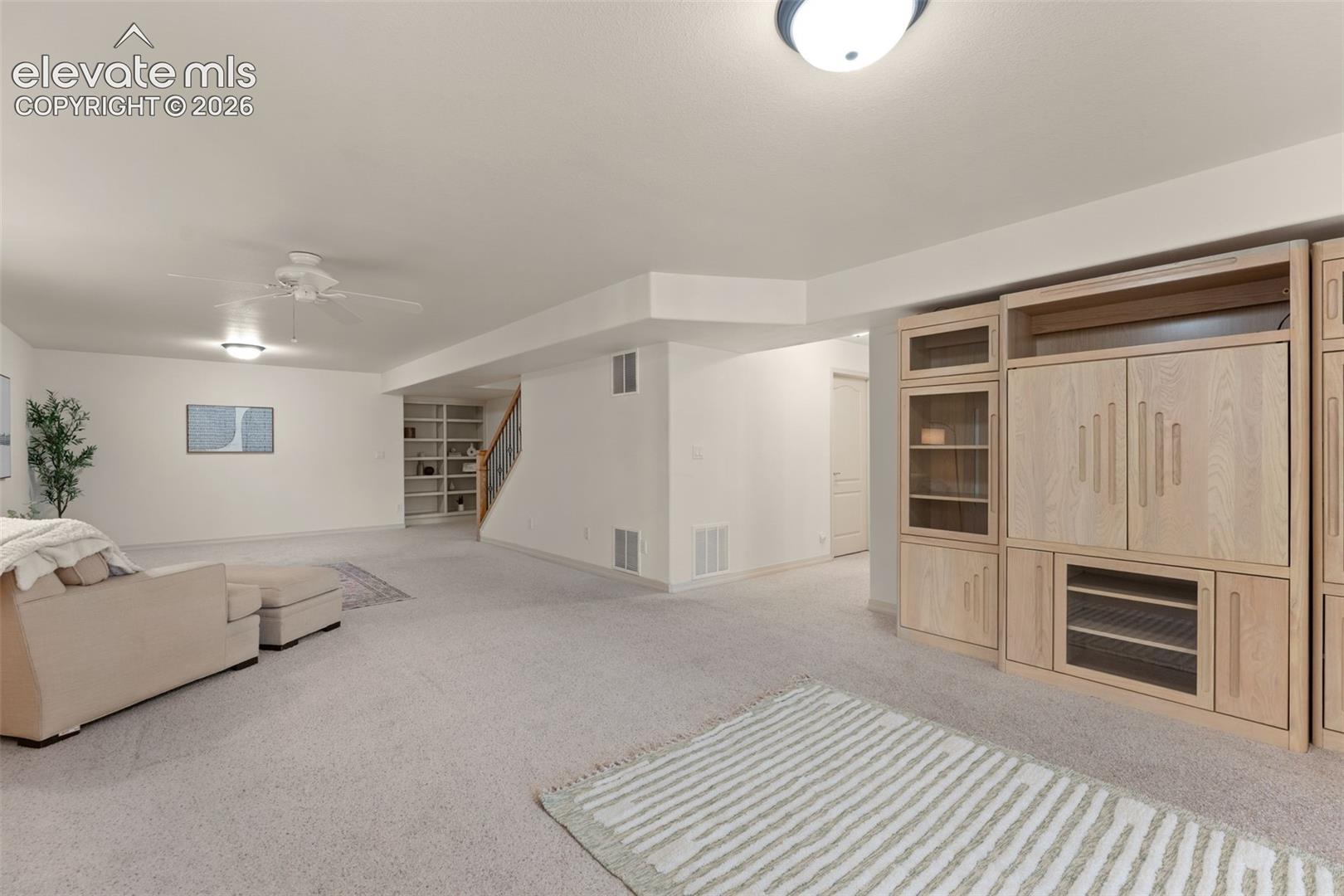Large open-concept interior featuring wall-to-wall carpeting, built-in light wood cabinetry, recessed shelving, and a ceiling fan
