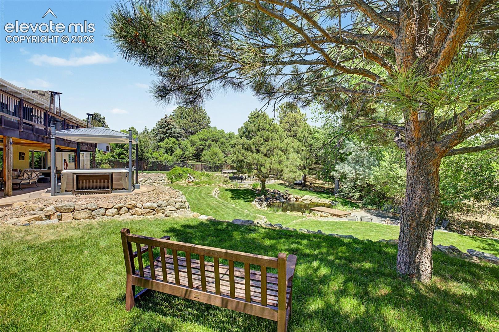 Beneath a towering pine offers the perfect vantage point to take in the backyard's pond, covered patio, and hot tub pergola — the kind of spot you'd want to sit and stay awhile.