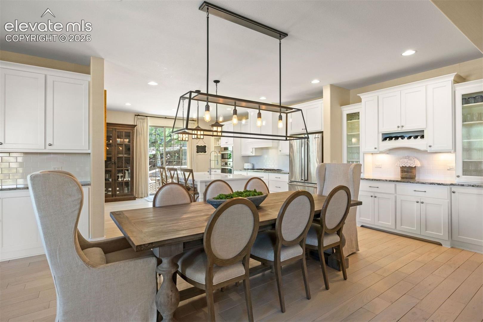 Dining area featuring a rectangular chandelier, light-toned wood-finish flooring, and white cabinetry