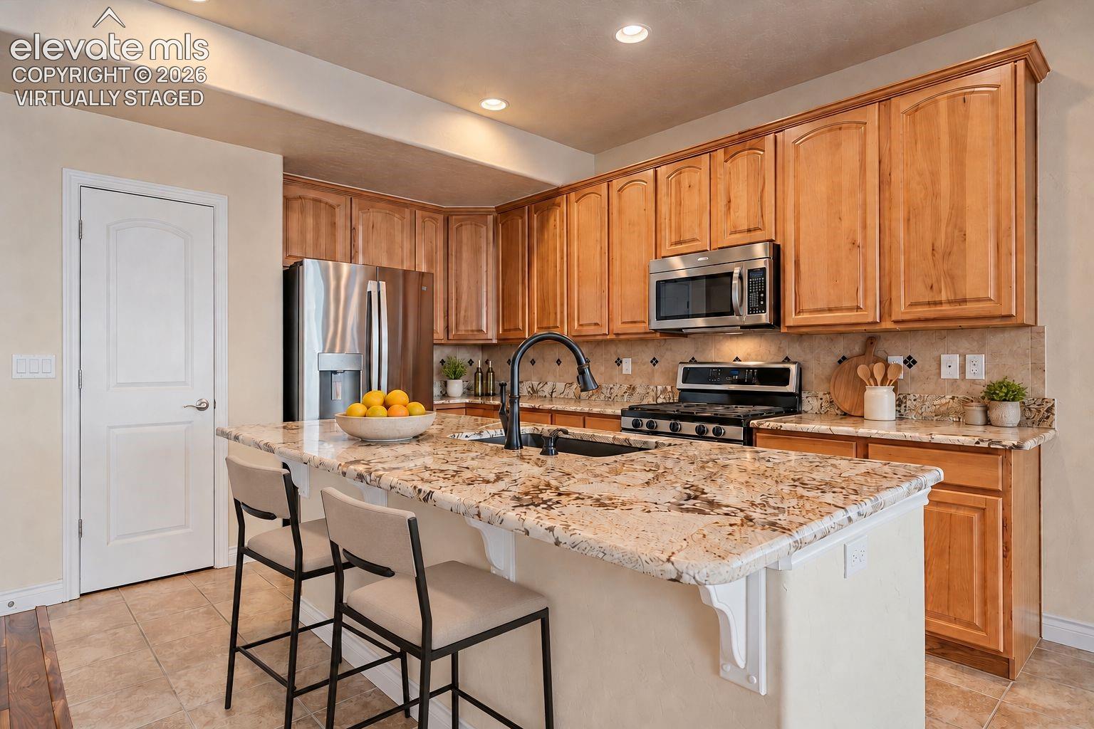 Virtually Staged. Kitchen featuring stained wood cabinetry, stone-finish countertops, stainless steel appliances, a center island with integrated sink, and recessed lighting