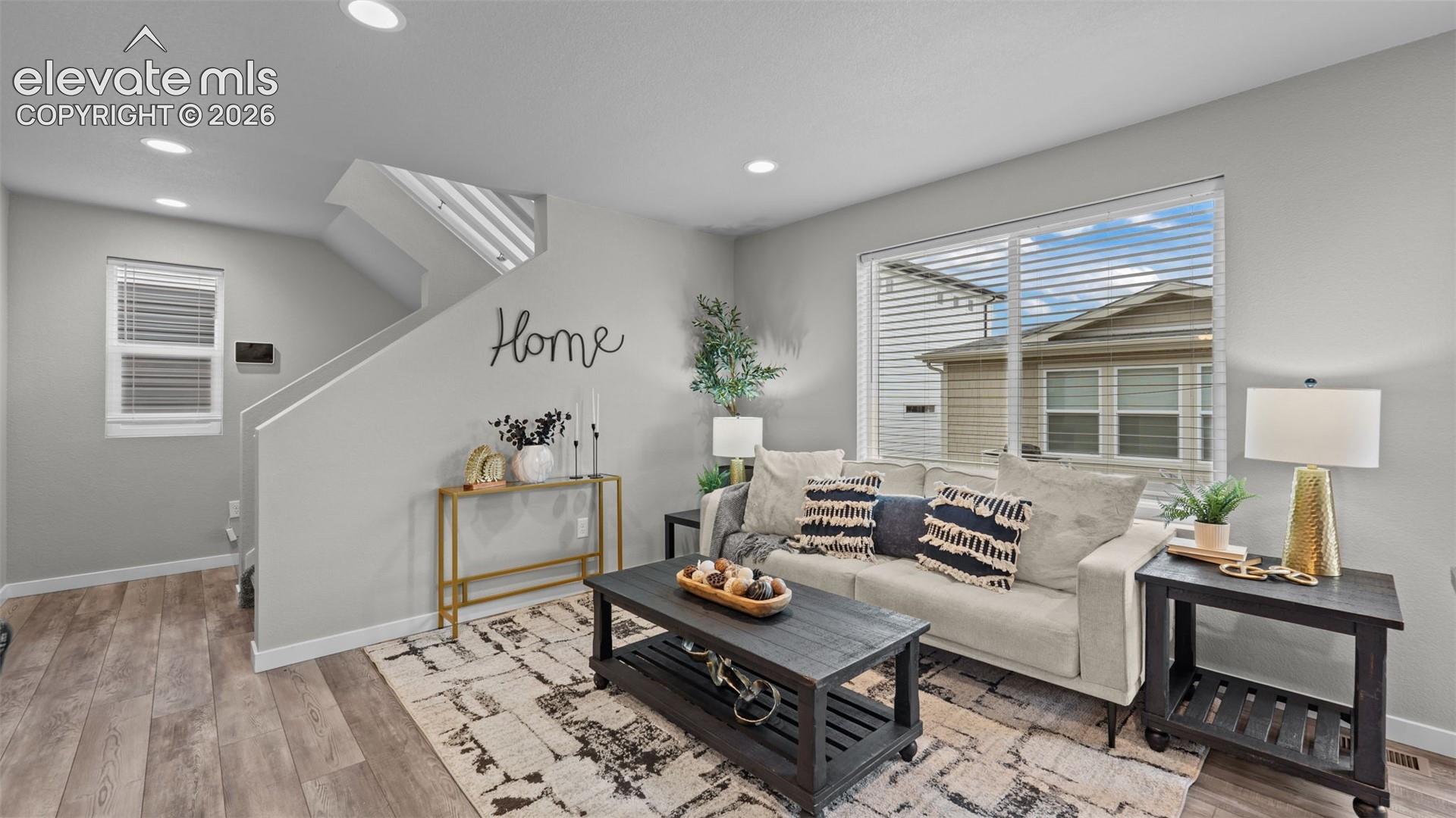 Living area featuring wood-finish flooring, recessed lighting, and a large picture window with blinds