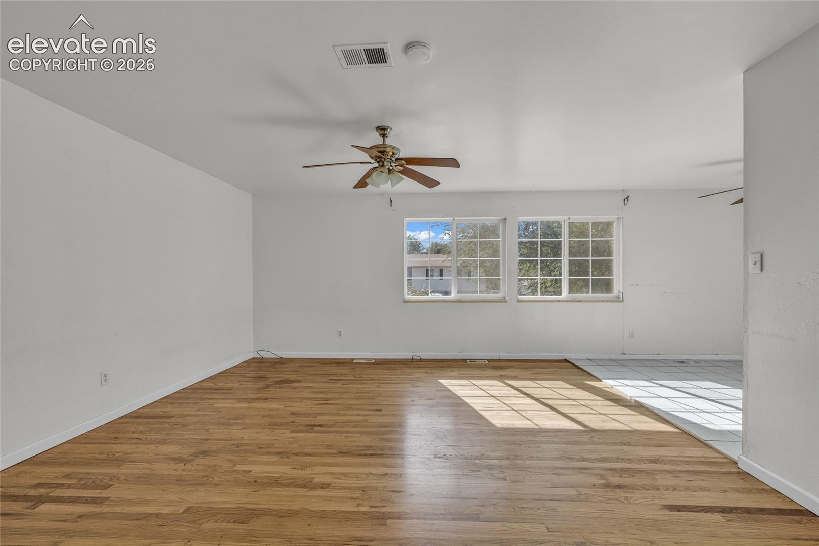 Expansive room featuring wood-finish flooring, white walls, and a ceiling fan