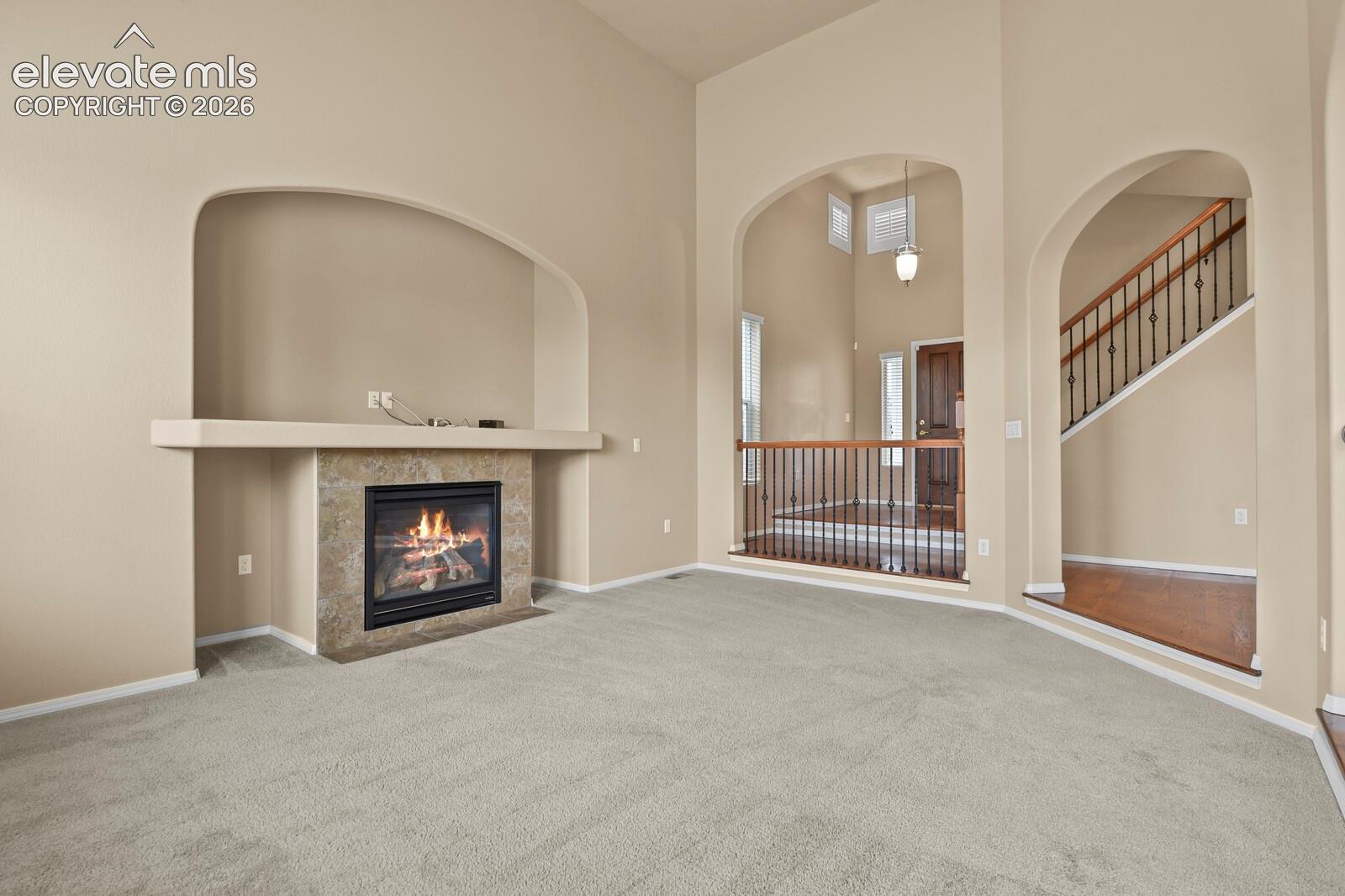 Arched doorways, a gas fireplace with a tiled surround, a built-in media niche, and a staircase with wrought iron balusters characterize this interior