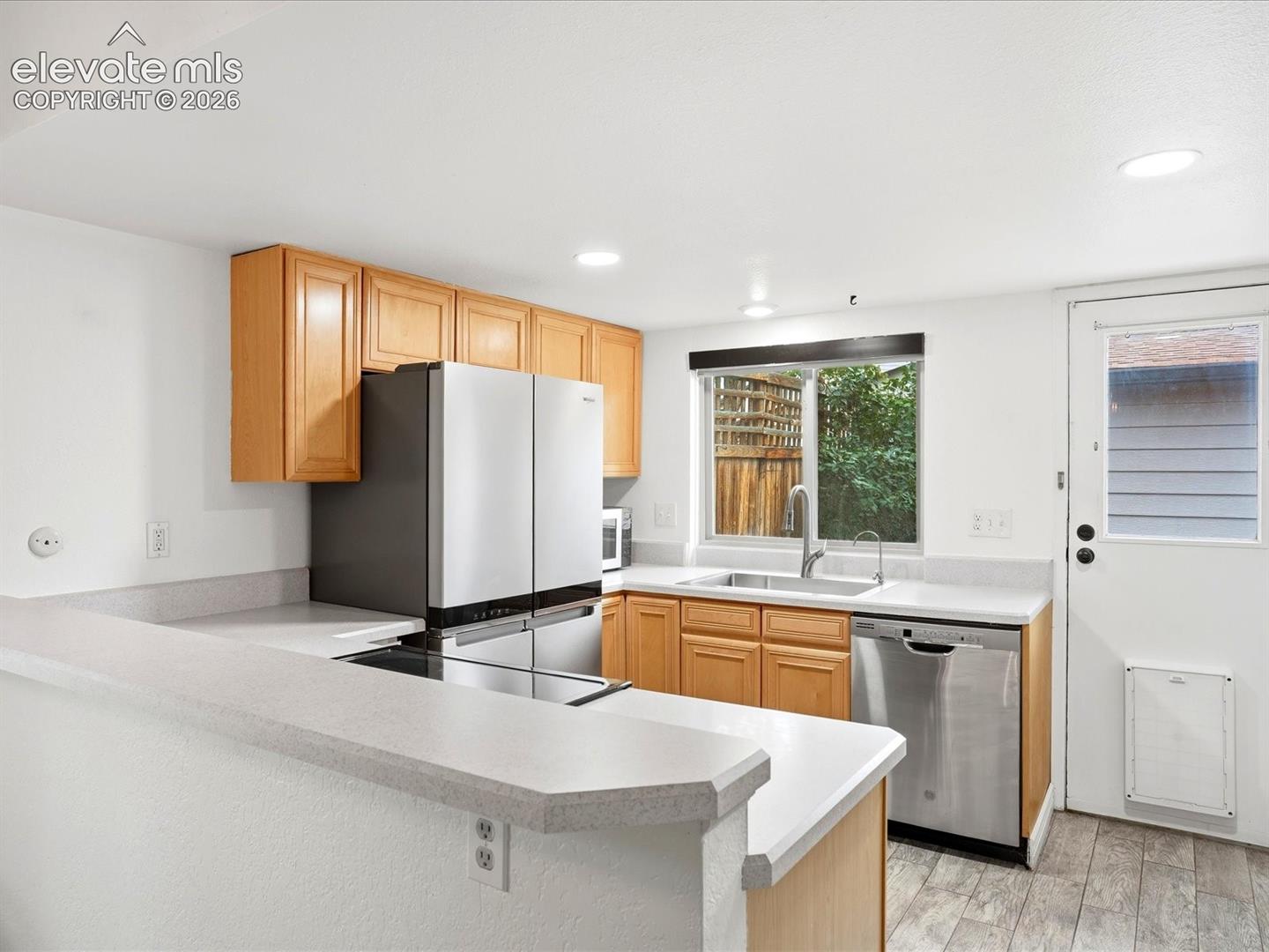 Kitchen featuring light-finish cabinetry, neutral solid-surface countertops, stainless steel appliances, a stainless steel sink with a pull-down faucet, and wood-finish flooring