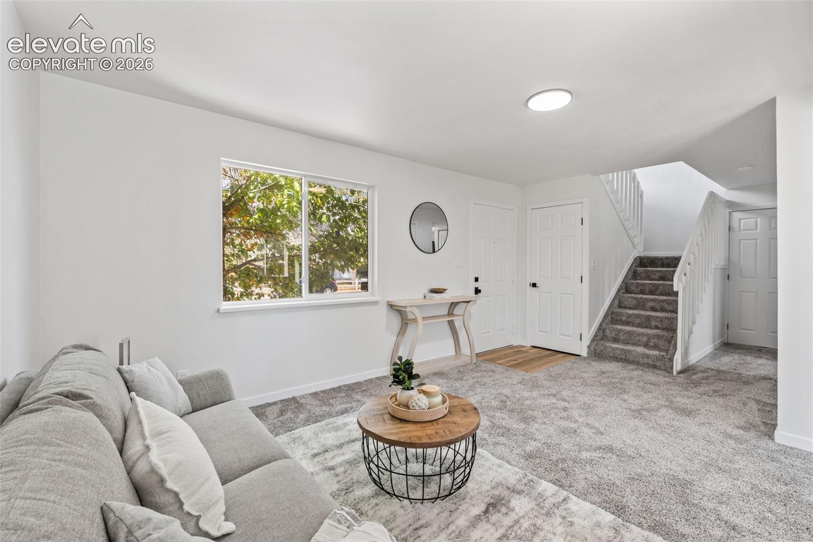Neutral-toned interior featuring wall-to-wall carpeting, a multi-pane window, staircase with white railing, and paneled interior doors