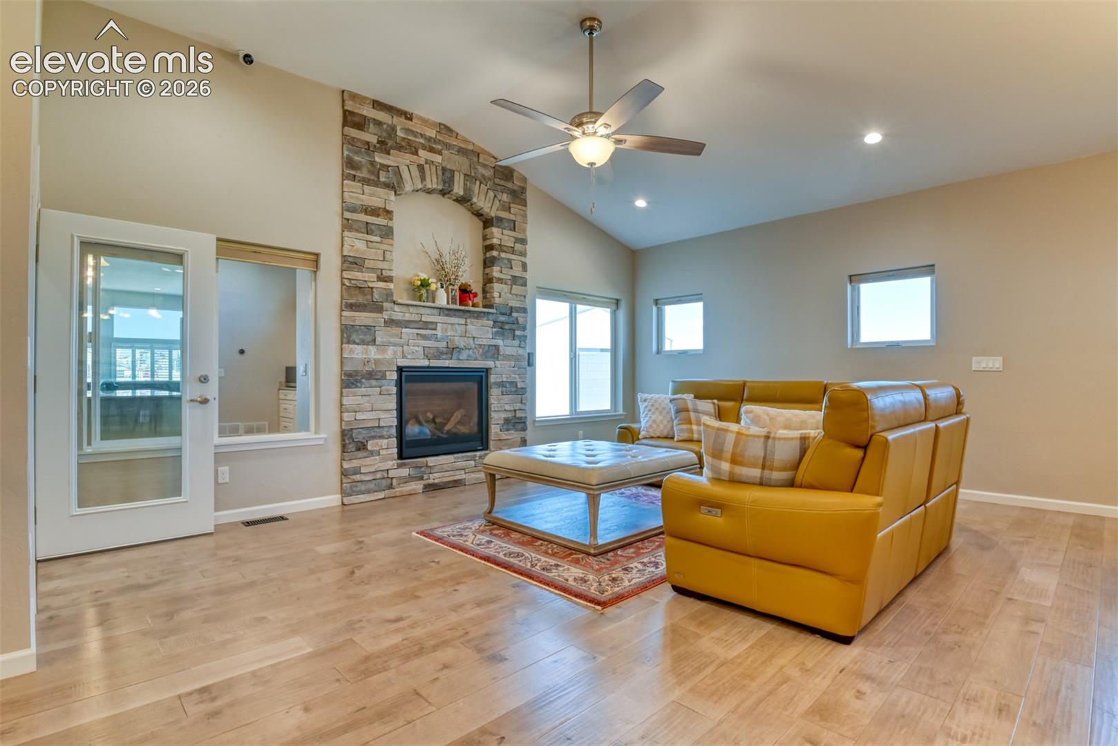 Vaulted ceiling with a ceiling fan, gas-log fireplace, wood-finish flooring, recessed lighting, and multiple windows.