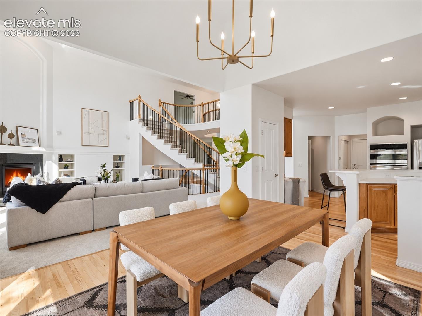 Open-concept interior featuring vaulted ceilings, a central staircase with a metal balustrade, a wood-burning fireplace with built-in shelving, wood-finish flooring, and recessed lighting