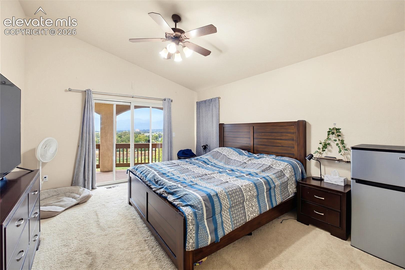 Vaulted ceiling with a ceiling fan, sliding glass door leading to a balcony, and carpeted flooring