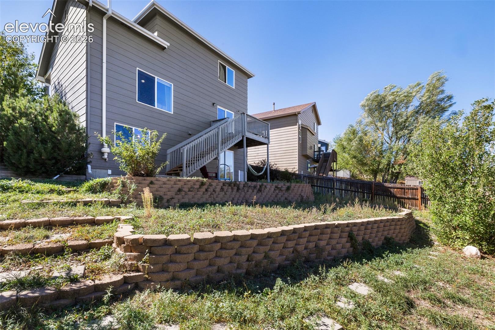 Exterior featuring horizontal siding, a raised wooden deck with stairs, and tiered stone block retaining walls