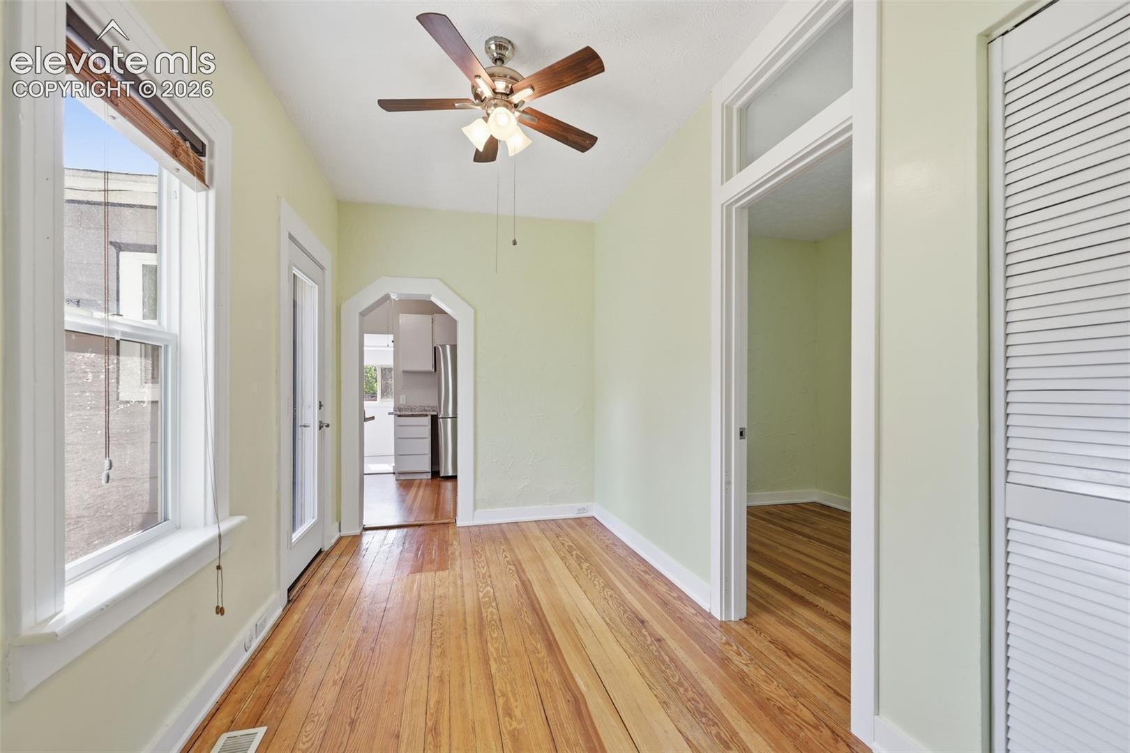 Dining area with pine hardwood flooring, arched opening, a ceiling fan, wooden blinds, white trim, and a glass-paneled side door.