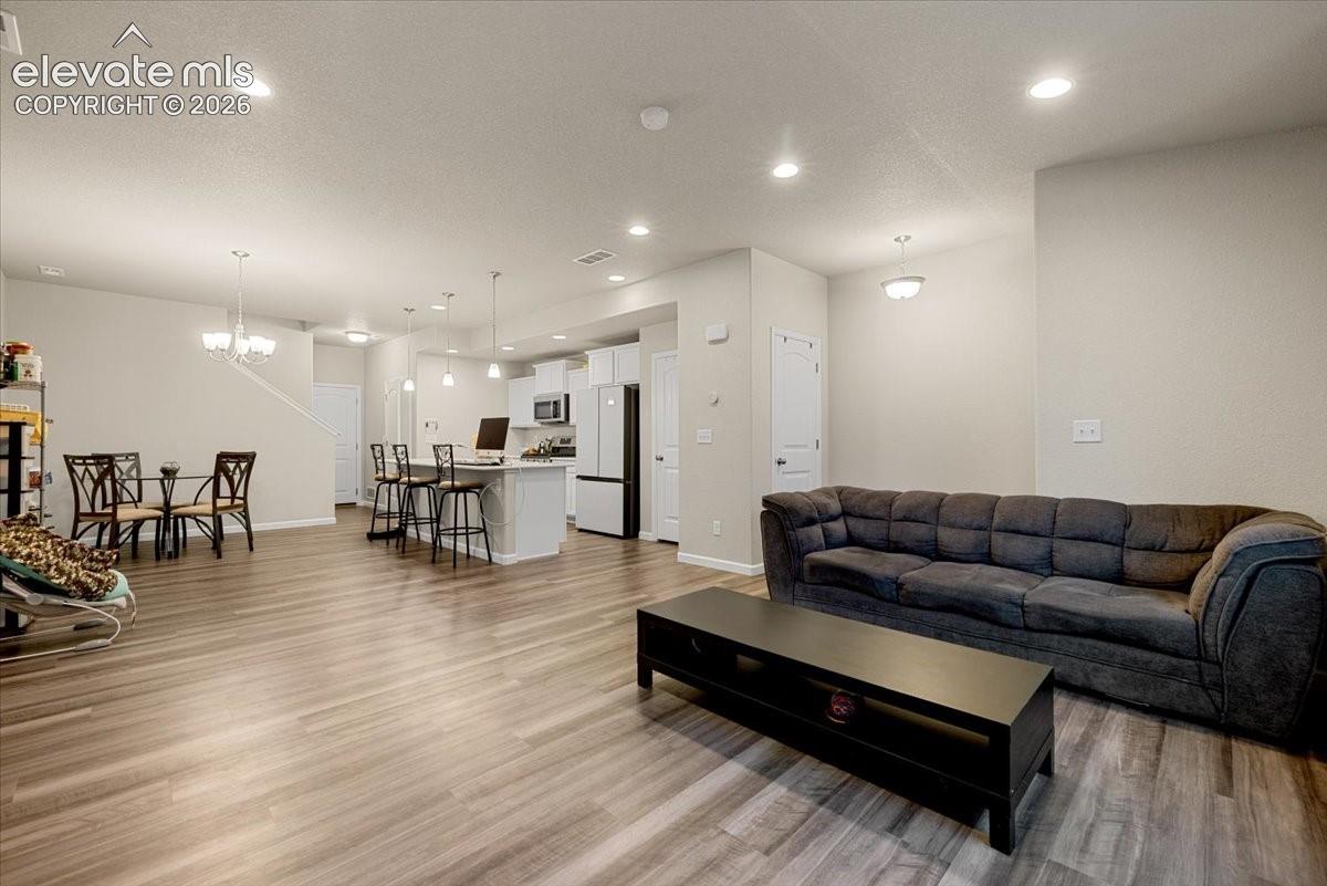 Open-concept living area with wood-finish flooring, recessed lighting, and a kitchen island with pendant lighting