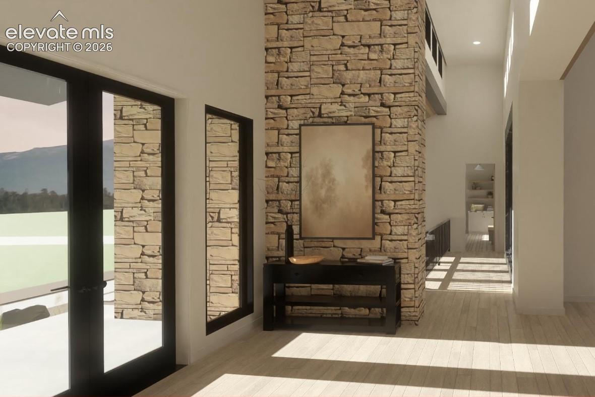Stone architectural feature with a high ceiling, wood-finish flooring, and expansive glass doors