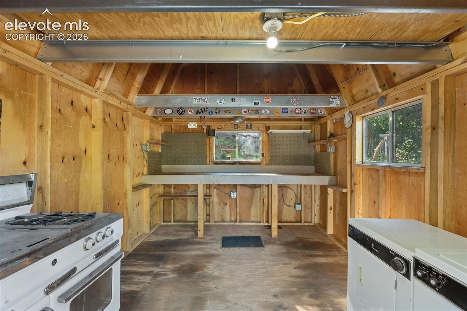Utility space featuring natural wood paneling, exposed beam ceiling, built-in workbench, and two windows
