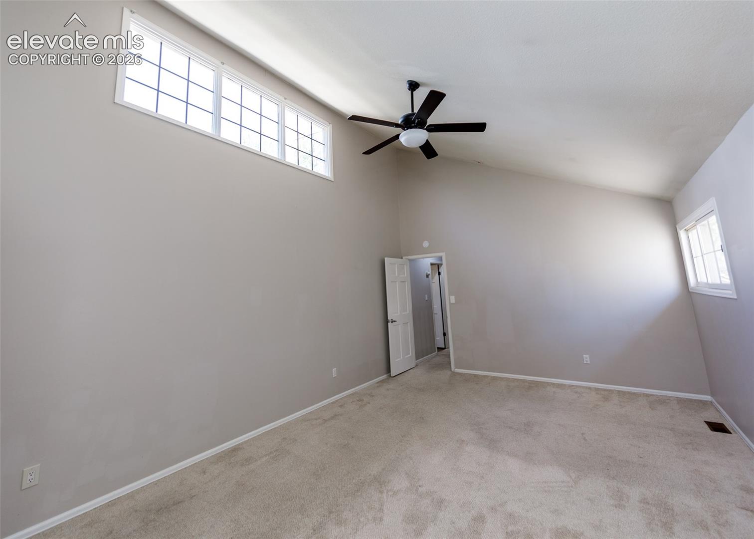 Vaulted ceilings, transom windows, neutral wall tones, carpet flooring, and a ceiling fan with integrated lighting