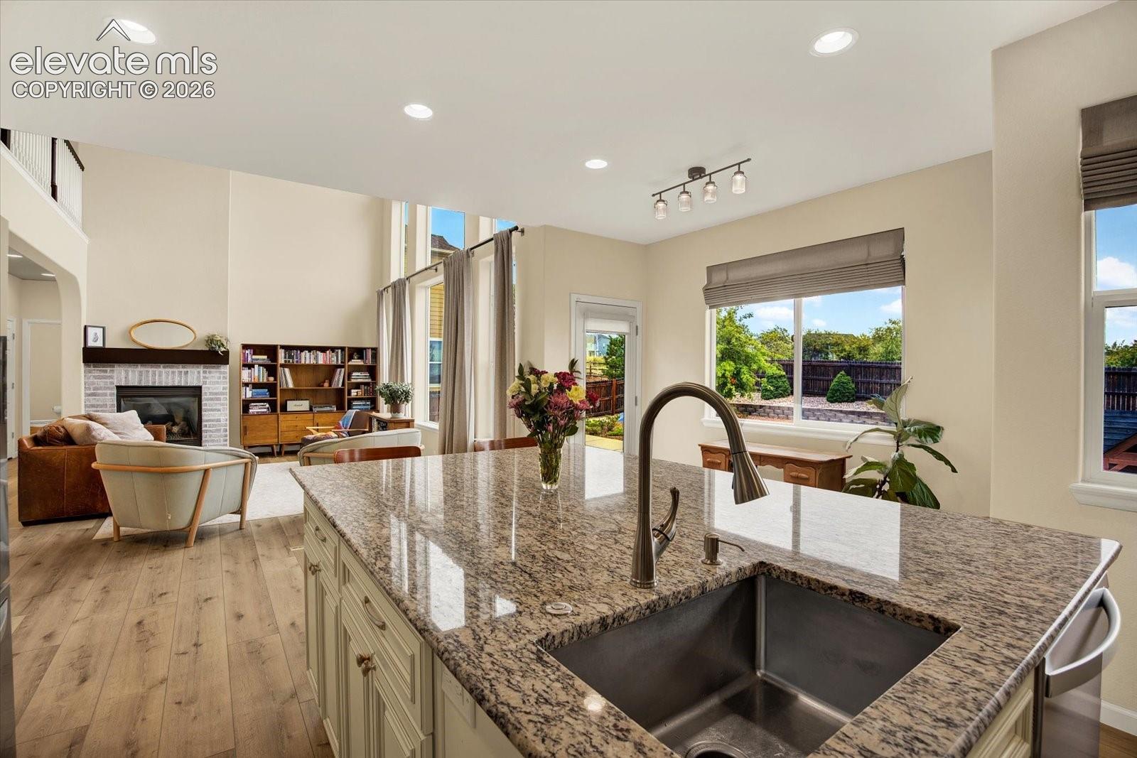 Kitchen featuring a center island with stone countertops, an undermount stainless steel sink, wood-finish flooring, recessed lighting, and a painted brick fireplace