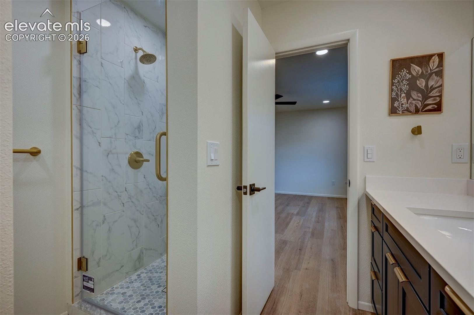 Walk-in shower with floor-to-ceiling tile, brass-finish fixtures, and a frameless glass door, paired with a vanity featuring a white countertop and dark-toned cabinetry