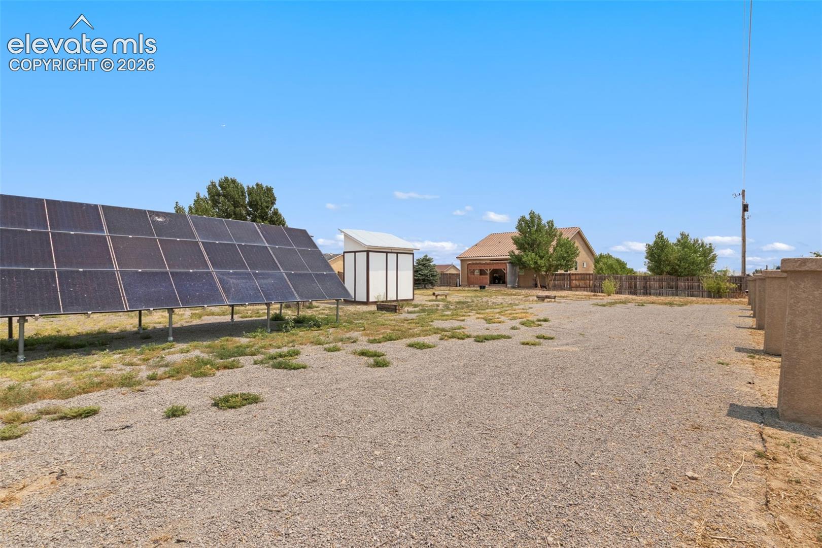 Ground-mounted solar panel array, gravel lot, detached storage structure, and perimeter fencing