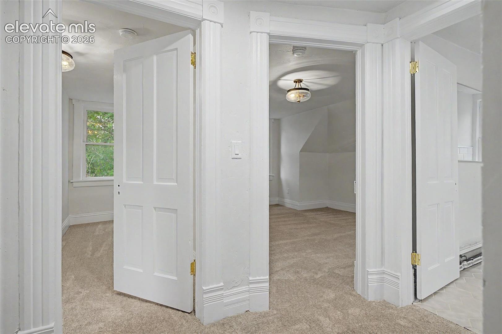 An interior hallway featuring three white paneled doors, light beige carpeting, and white trim