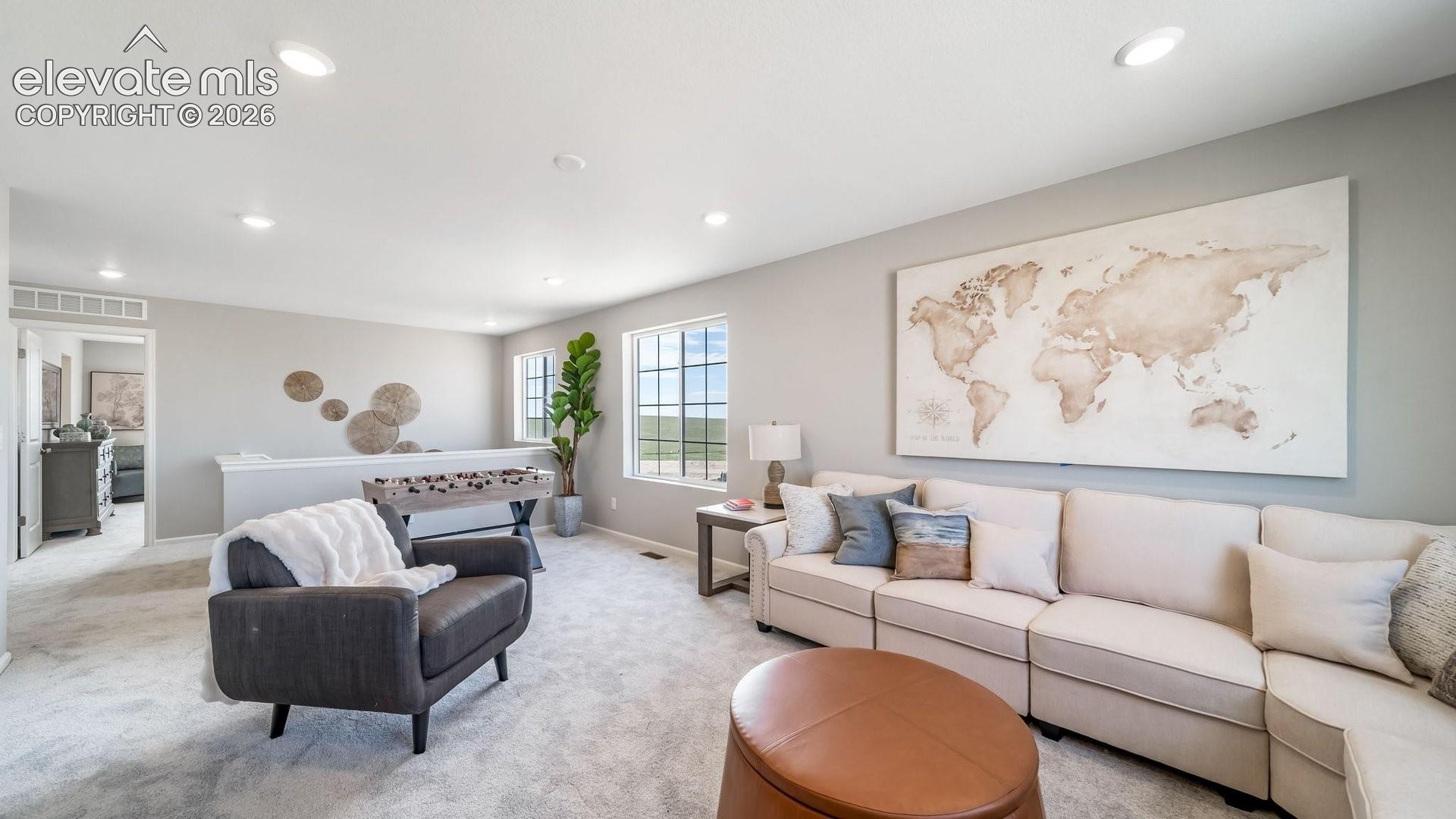 Expansive carpeted room featuring recessed lighting, multiple windows, and a partial wall with a railing
Photos of a model home