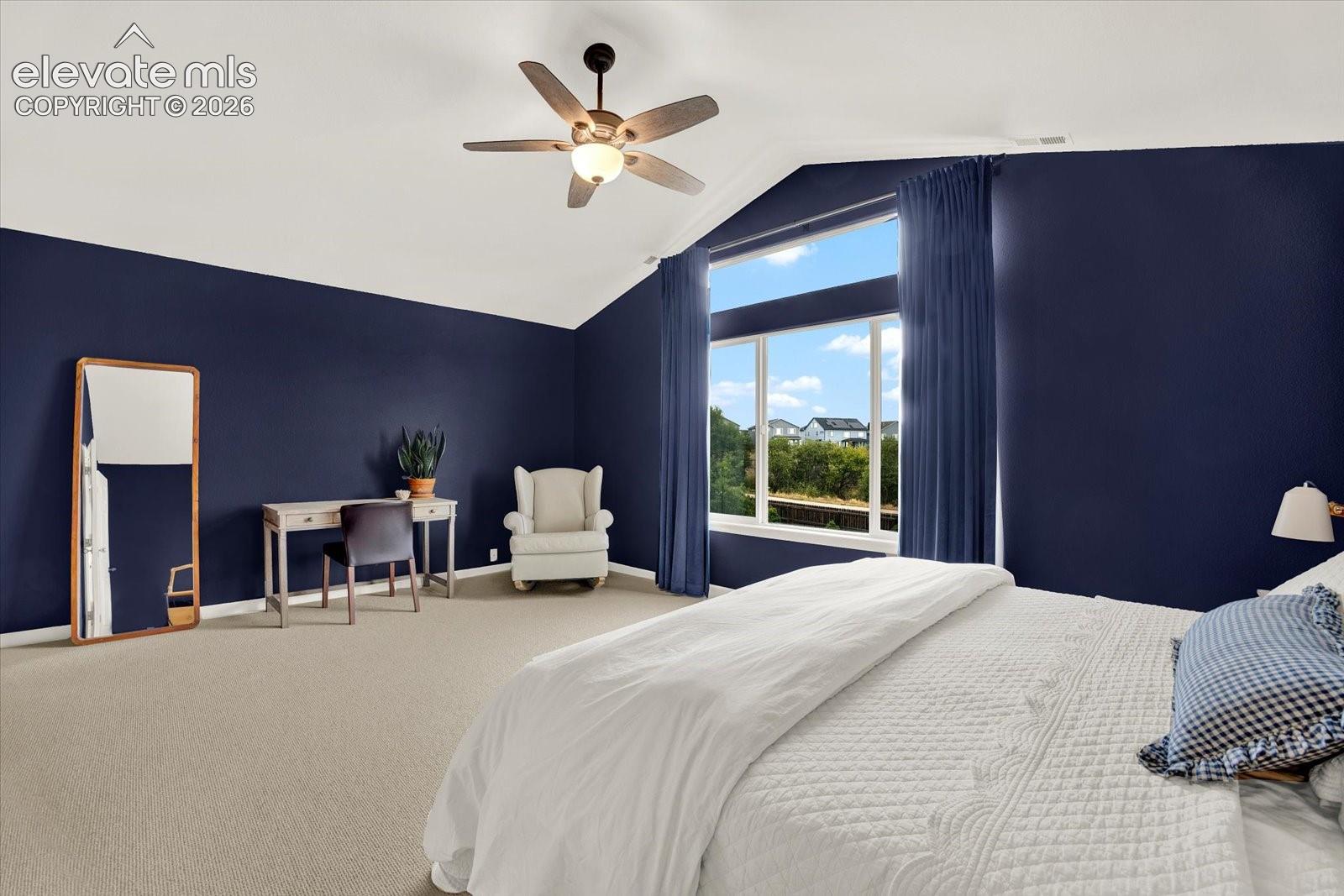 Vaulted ceiling featuring a central multi-blade ceiling fan with integrated lighting, large picture window with transoms, and neutral carpeting