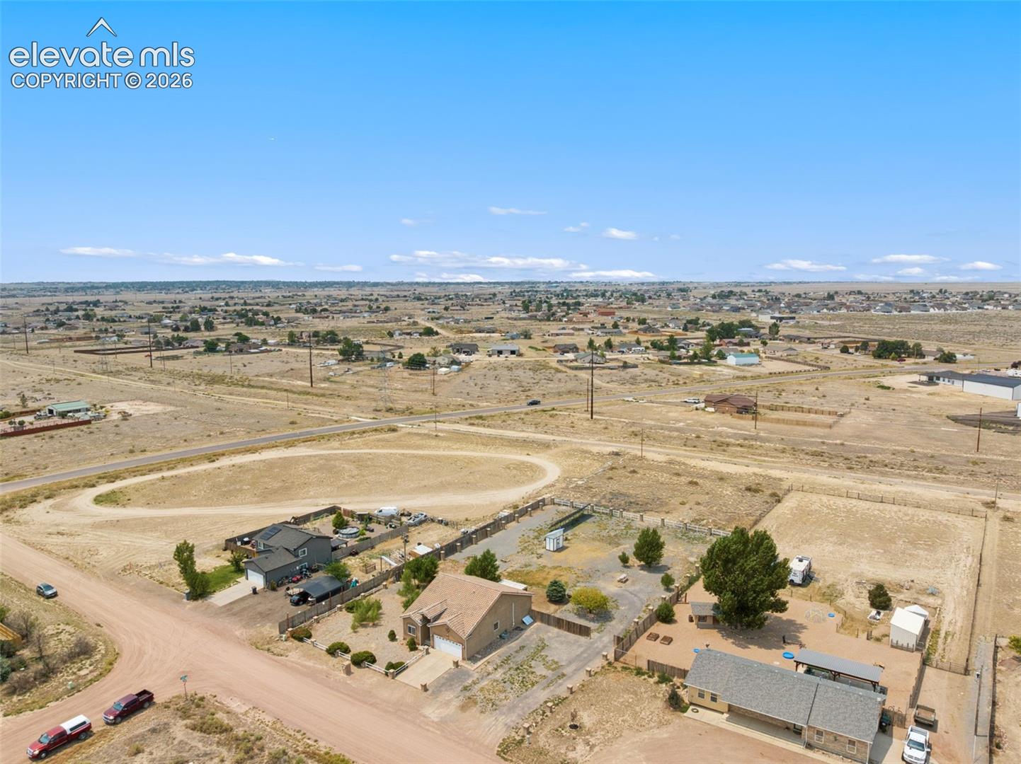 Aerial perspective of a detached residential property featuring a paved driveway, attached garage, and expansive lot with desert landscaping