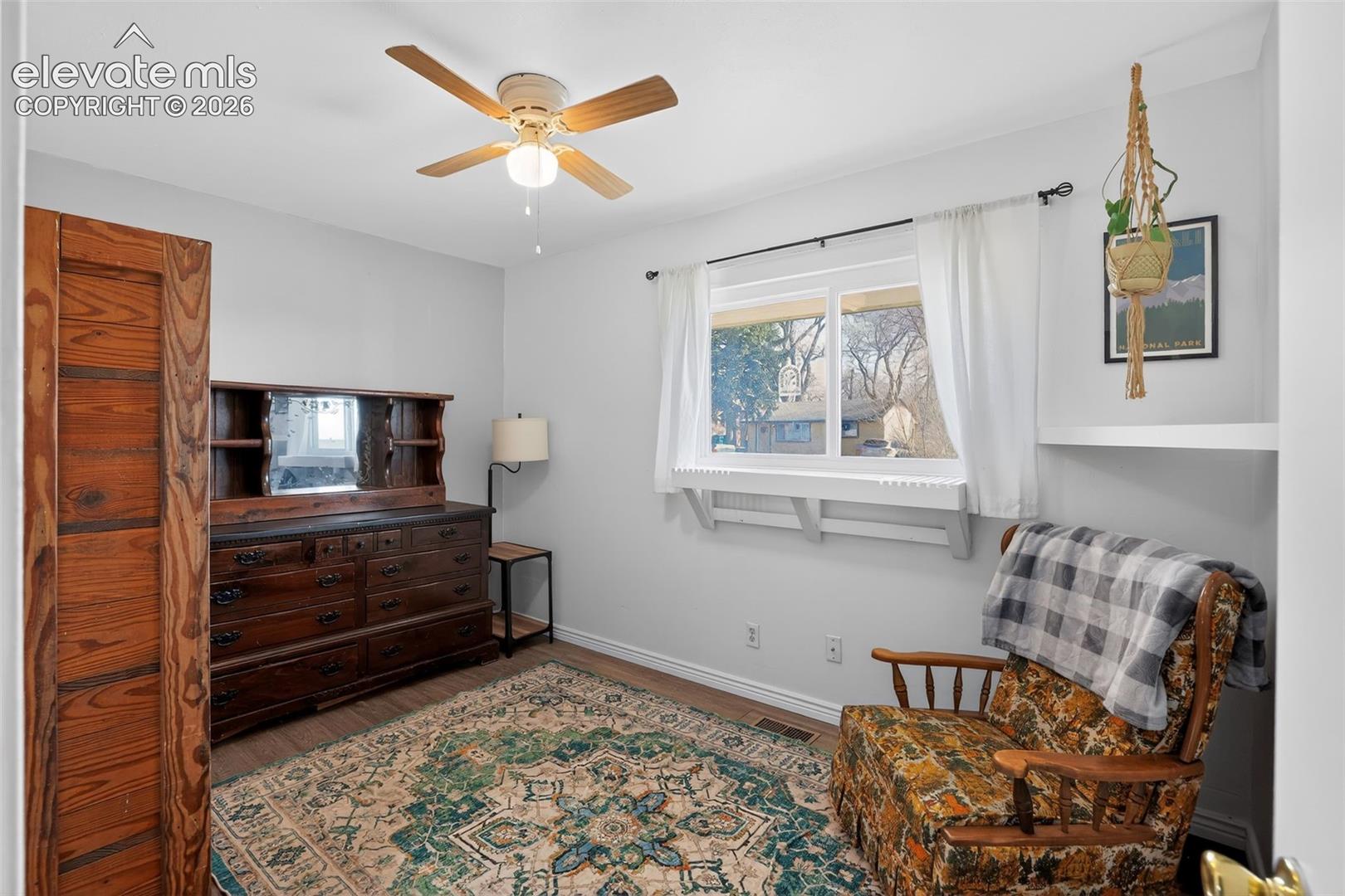 Wood-finish flooring, ceiling fan, and large window with white trim