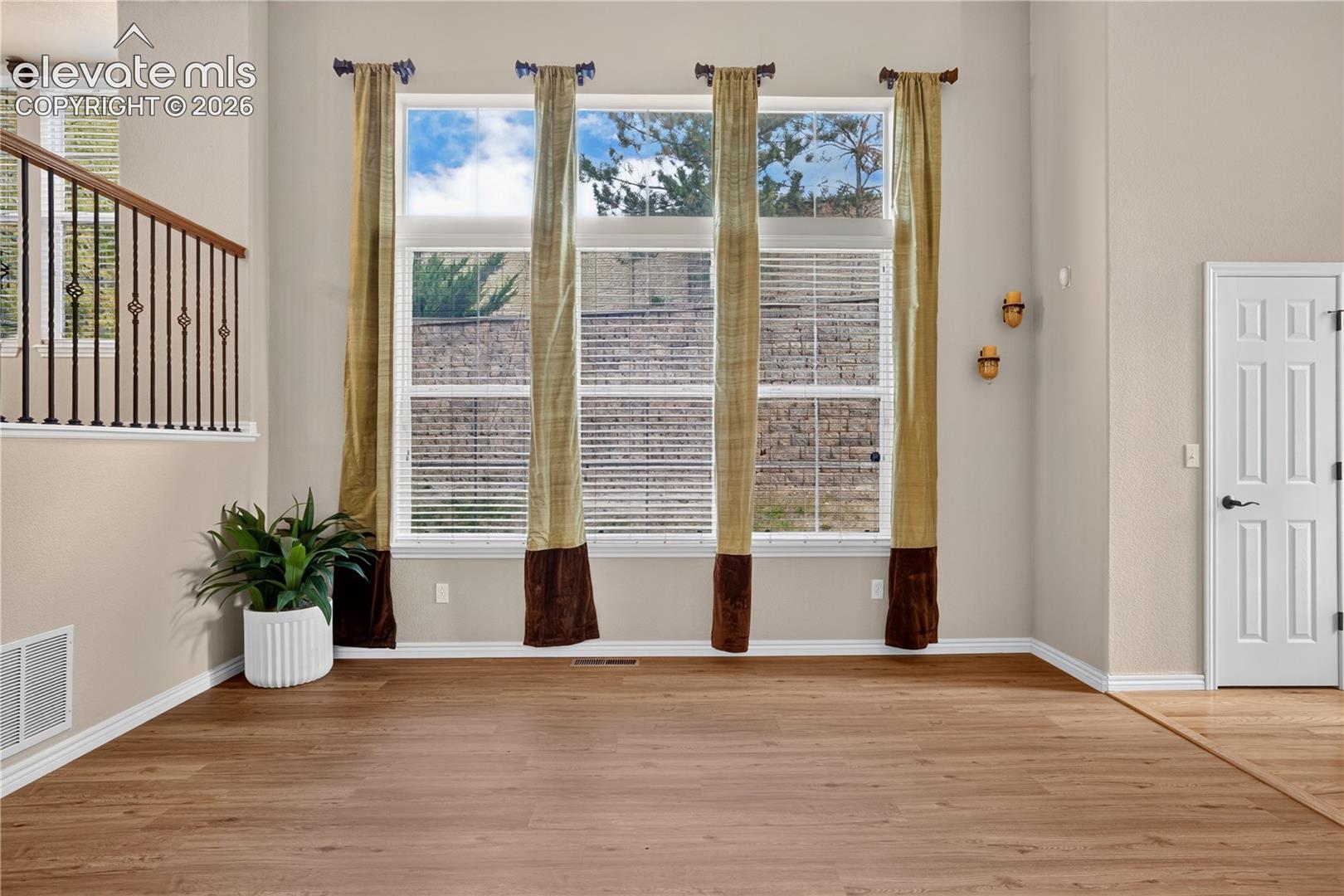 High-ceiling interior featuring a floor-to-ceiling grid of windows, wood-finish flooring, and a metal-spindle staircase railing. First tier of the main level.