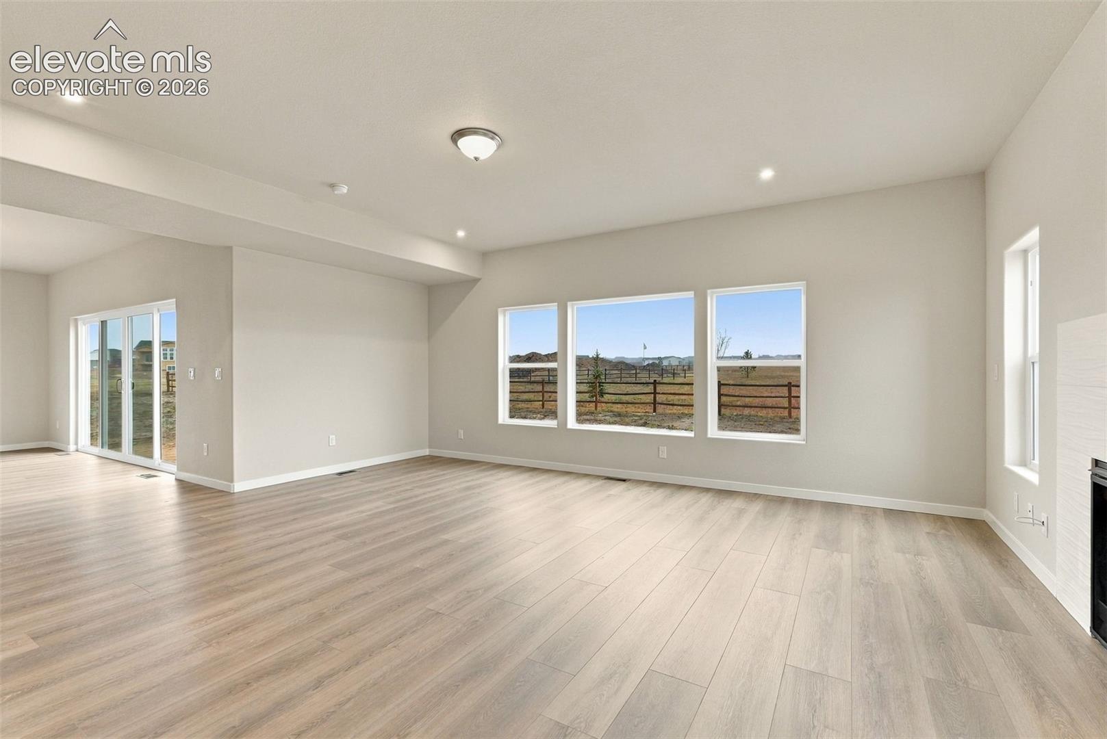 Open-concept living space featuring wood-finish flooring, recessed lighting, triple-pane windows, sliding glass door, and a white brick-surround fireplace