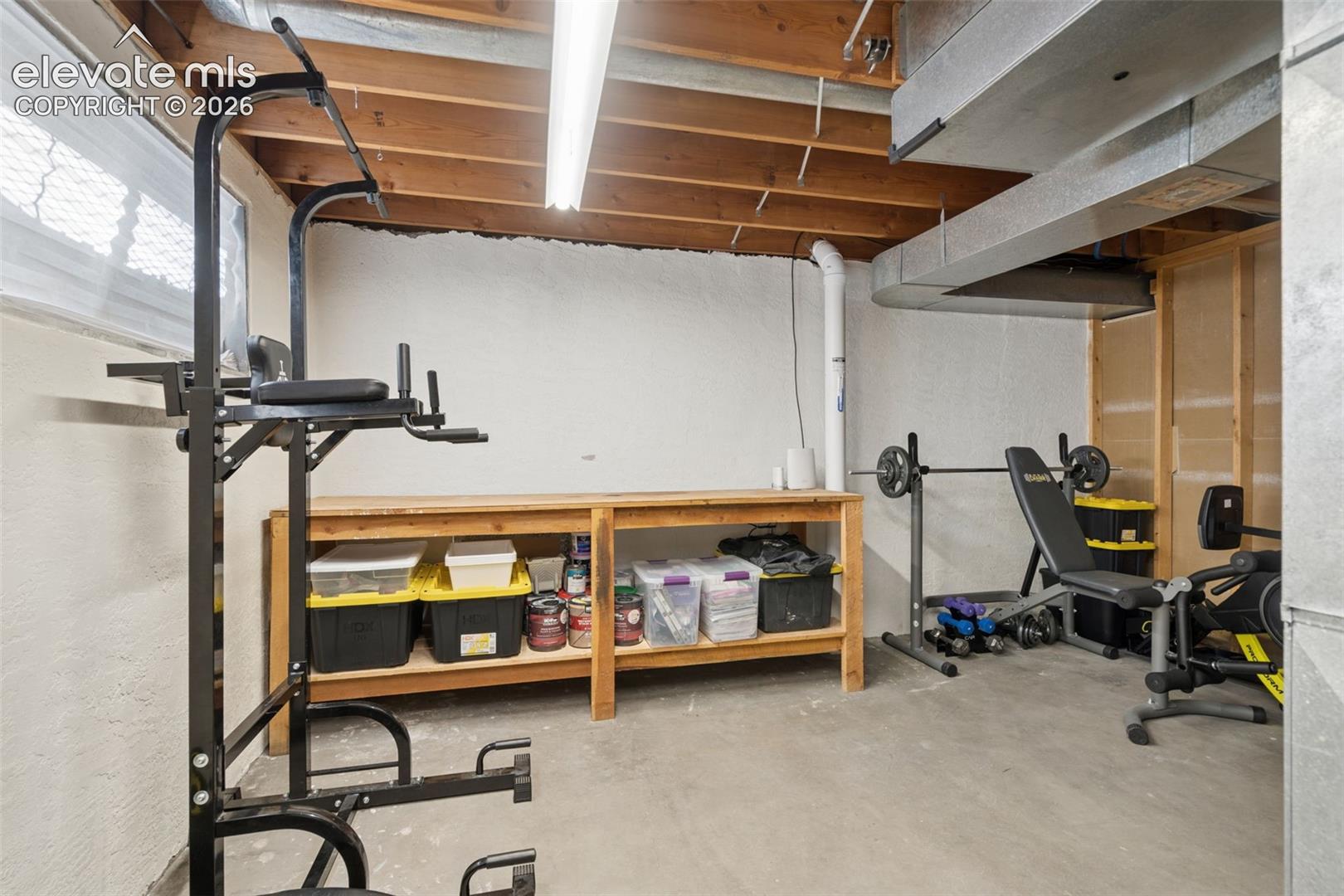 Basement Unfinished room featuring painted masonry walls, exposed ceiling joists, concrete flooring, and built-in wood shelving