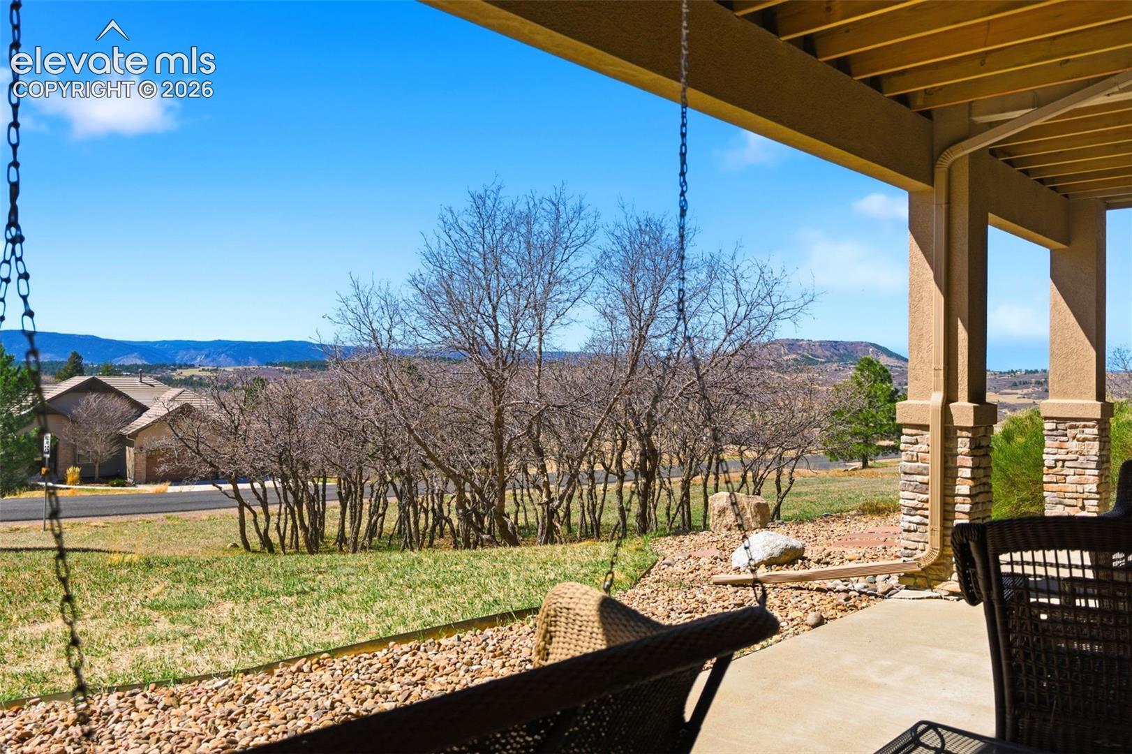 Covered patio with a concrete surface, stone-clad columns, and a natural landscape
