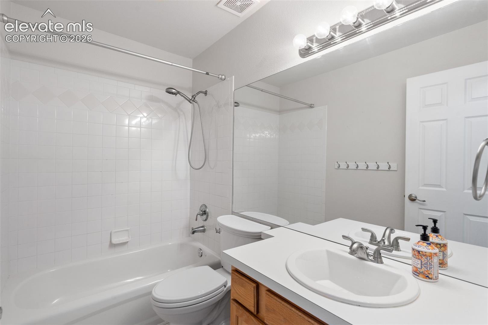 Full-width vanity featuring an integrated sink, polished chrome faucet, expansive wall-mounted mirror, and a tiled shower-tub combination with a handheld shower head