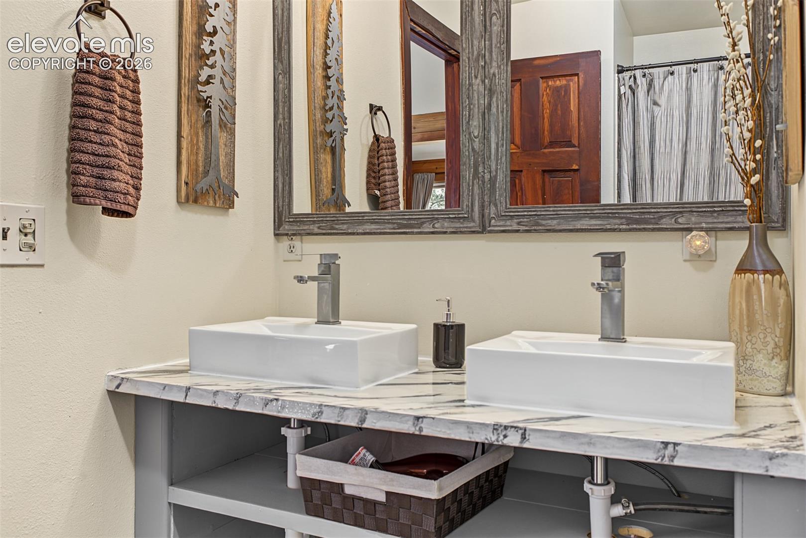 Dual vessel sinks with chrome-finish faucets, set on a patterned countertop with open shelving