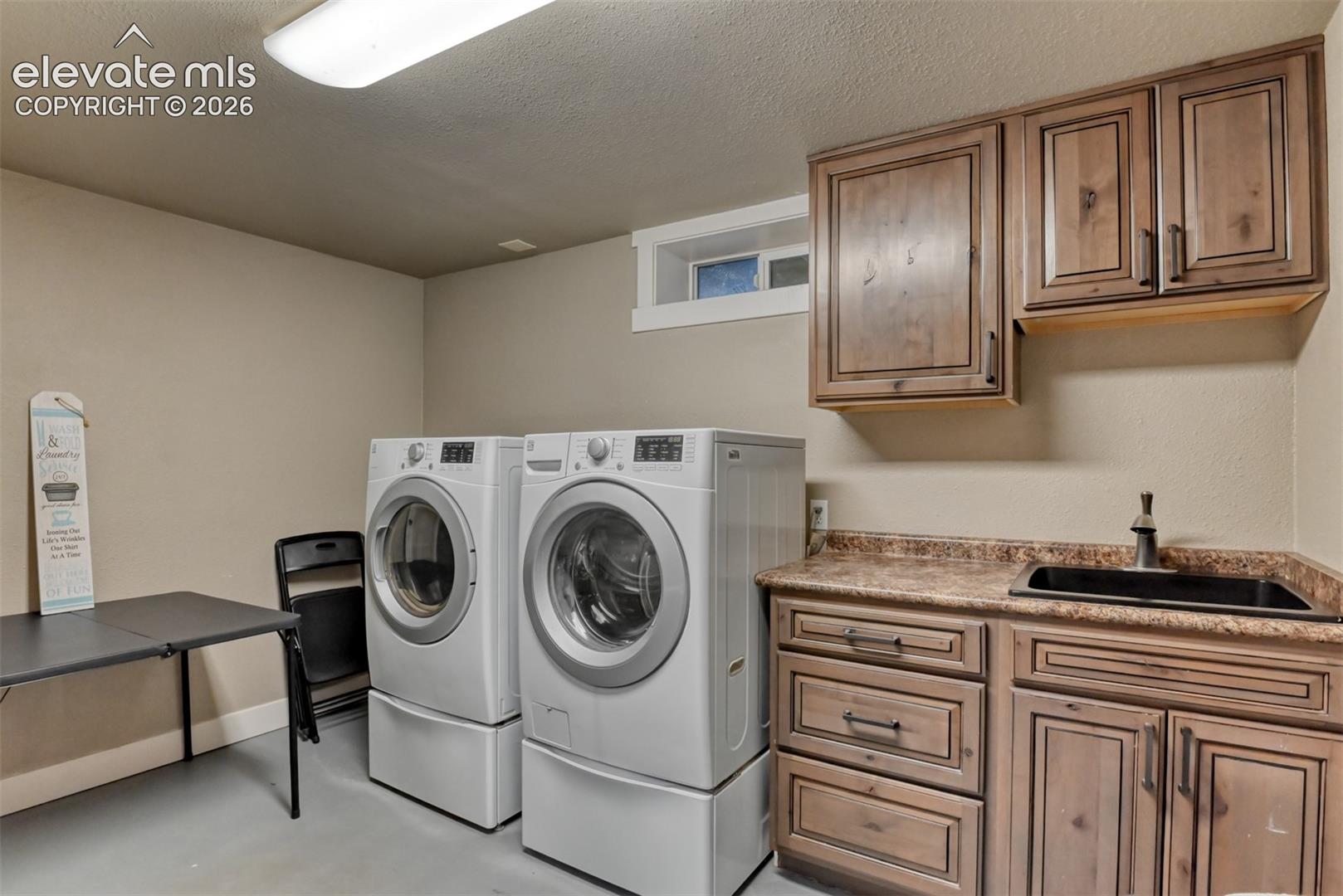 Laundry area featuring a textured ceiling, separate washer and dryer, concrete floors, and cabinet space