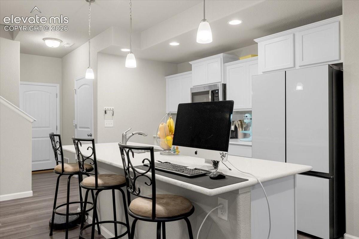 Kitchen island with a white countertop and integrated sink, stainless steel faucet, white upper and lower cabinetry, and recessed ceiling lighting