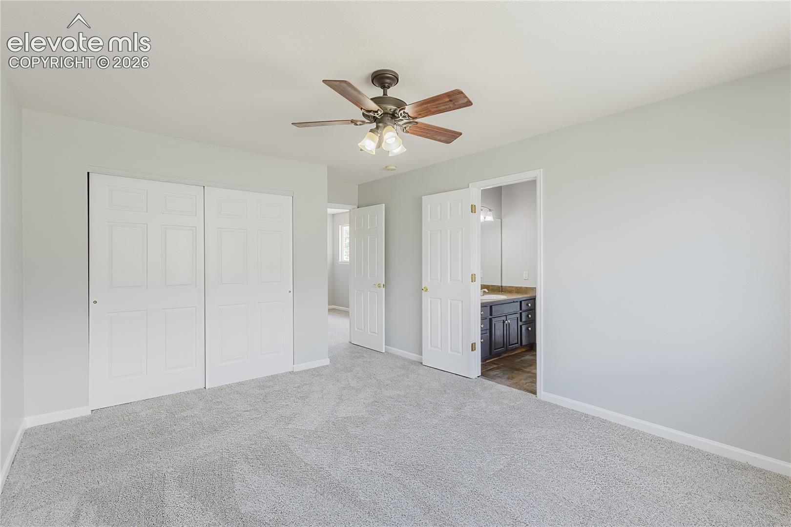 Carpeted room with a ceiling fan, bifold closet doors, and a doorway to a bathroom featuring a vanity with a countertop