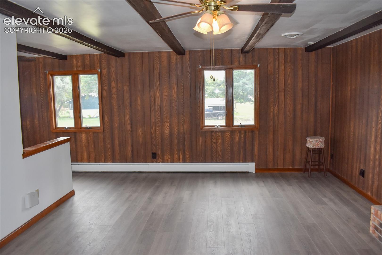 Wood-finish paneling, exposed ceiling beams, ceiling fan with integrated lighting, wood-finish flooring, and multiple windows