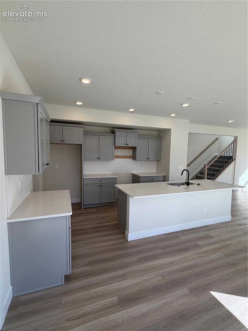 Kitchen featuring gray cabinetry, a central island with a sink, stone-finish countertops, recessed lighting, and wood-finish flooring