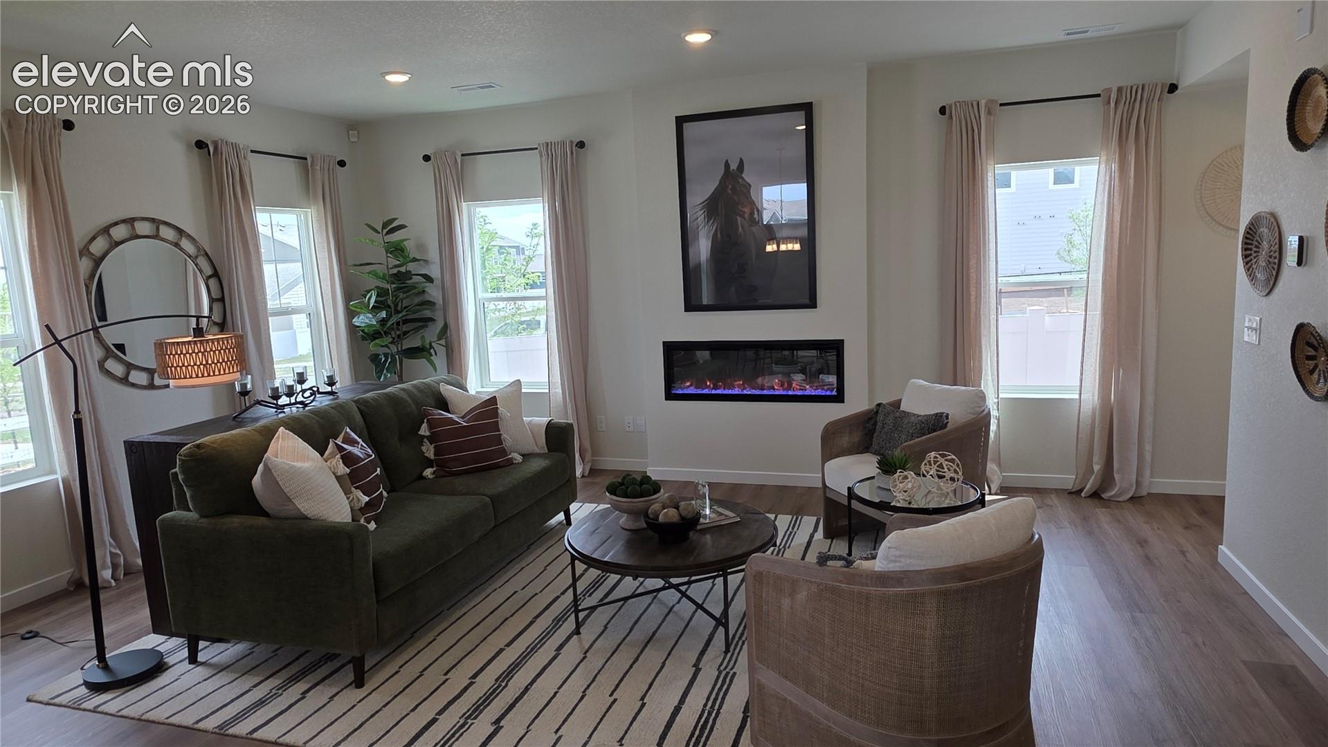 living room with recessed wall electric fireplace, large framed horse artwork, and three tall windows with curtains