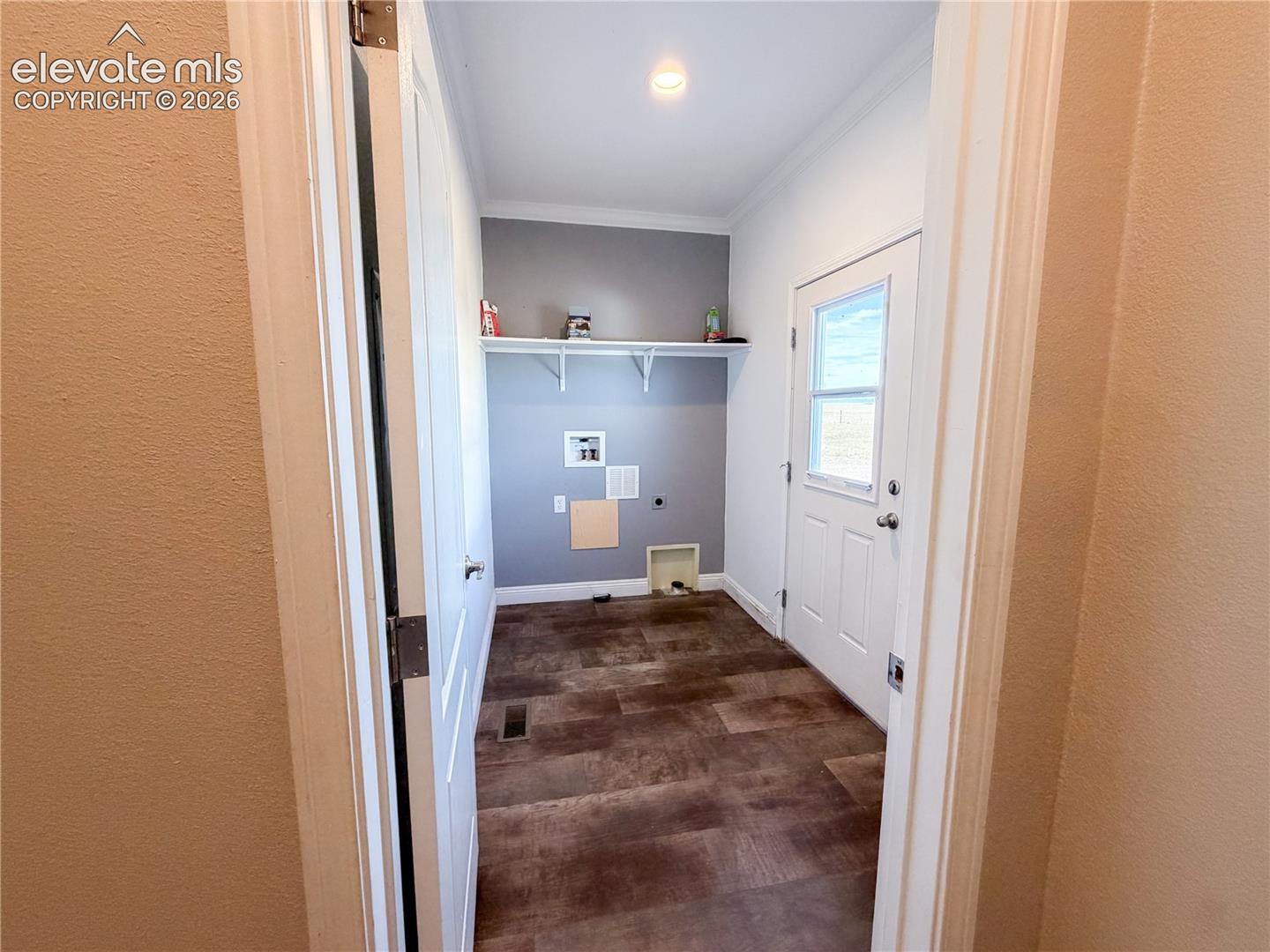 Utility space featuring wood-finish flooring, a wall-mounted storage shelf, and a white exterior door with a glass pane