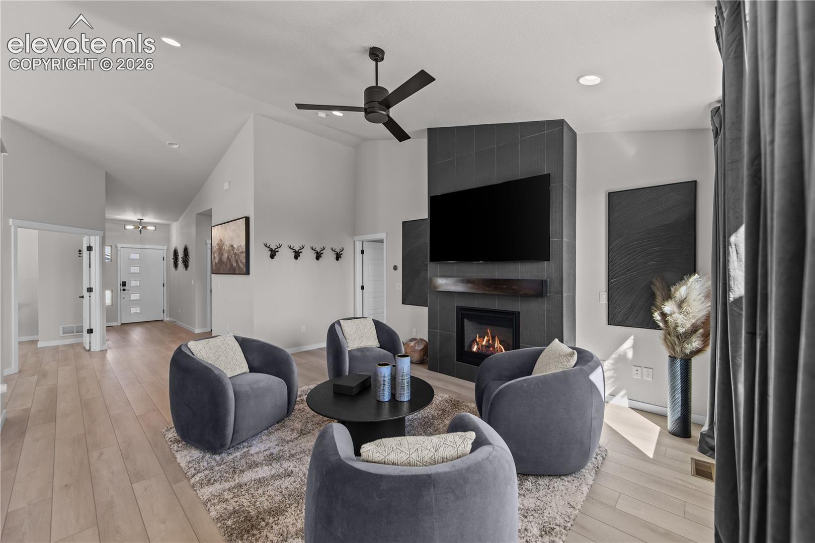 Vaulted ceilings, wood-finish flooring, floor-to-ceiling tile fireplace surround, and a dark wood mantel