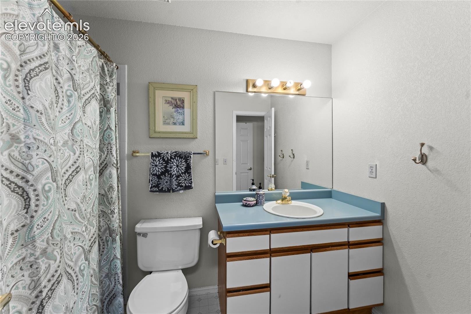 Full vanity mirror with overhead bar lighting, single basin sink, and a wood-finish cabinet with white panel doors and drawers