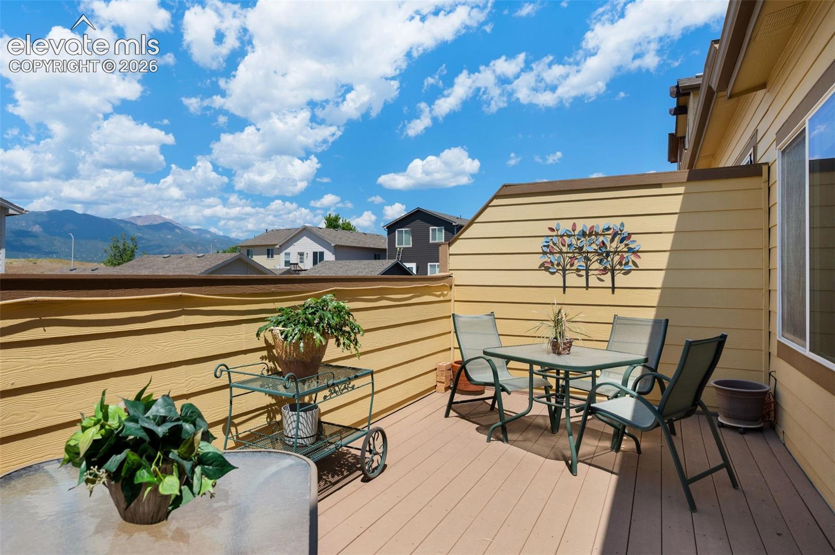 Expansive outdoor deck featuring wood-finish flooring, privacy walls, and mountain scenery including Pikes Peak.