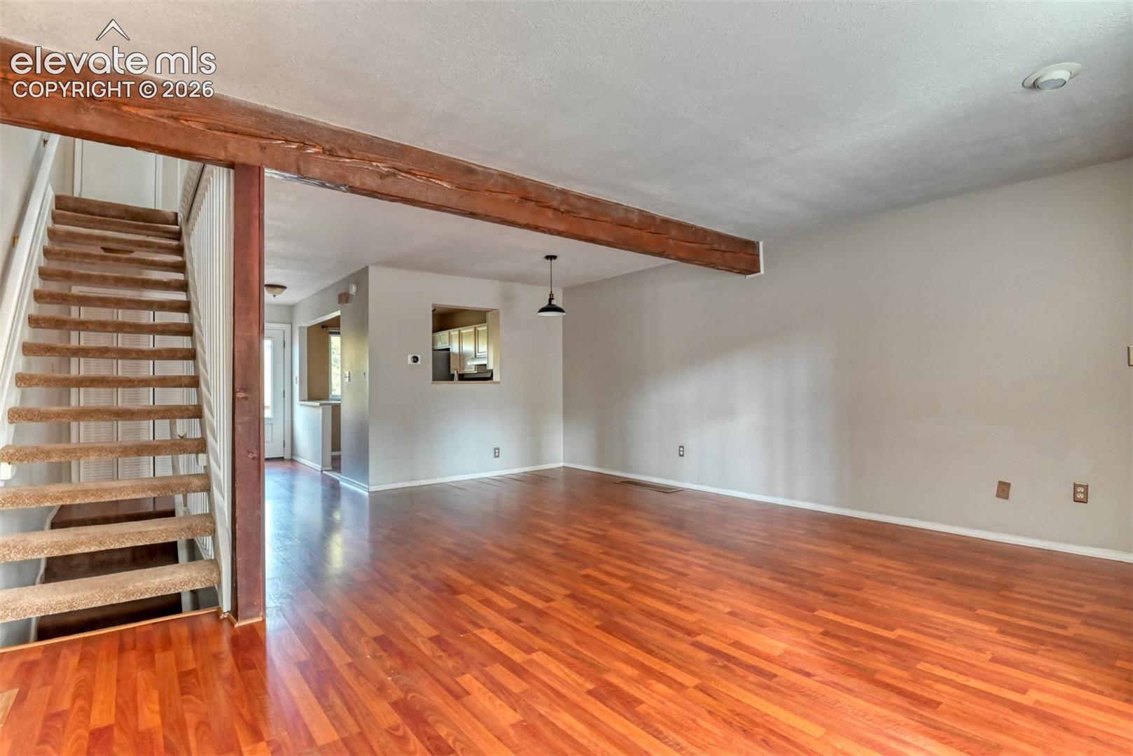 Hardwood-style flooring throughout, exposed wood beam, stairway with carpeted treads, and a pass-through window