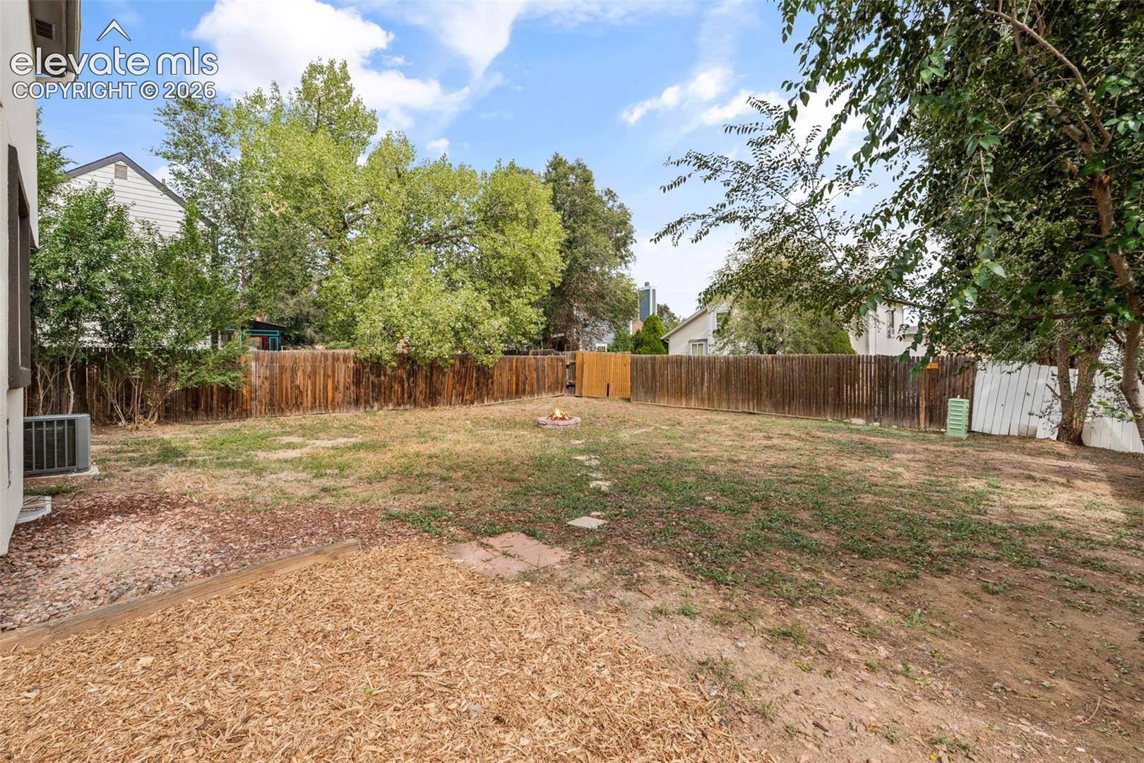 Backyard featuring a wood privacy fence, stone fire pit, wood-chip ground cover, and mature trees