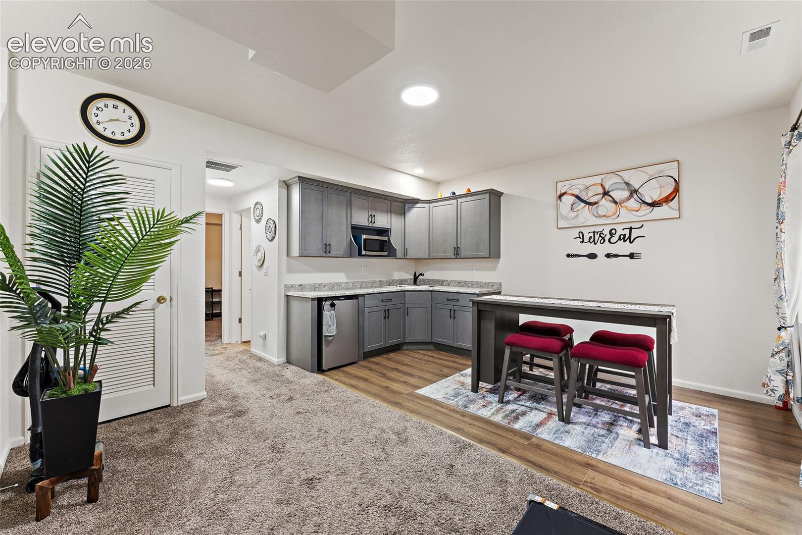 Kitchenette featuring grey cabinetry, stone-finish countertops, an under-counter refrigerator, a built-in microwave, and wood-finish flooring